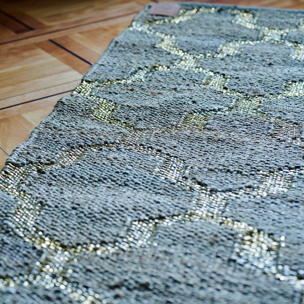 Der handgewobene Teppich wird in Rajasthan aus Jute gefertig. Der Teppich ist in zwei verschiedenen Farben, silber und gold, erhältlich. Durch sein natürliches Material kann das Produkt leichte Farbabweichungen aufweisen.